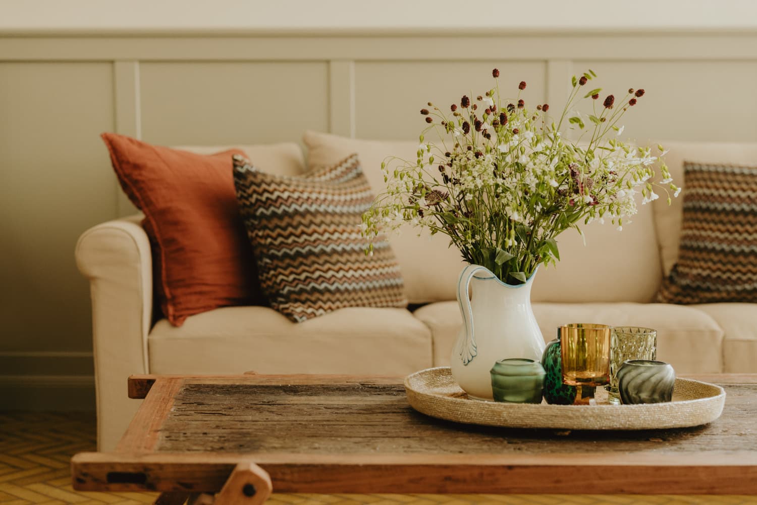 Sofa mit Kissen und Vase mit Wildblumen auf rustikalem Tisch